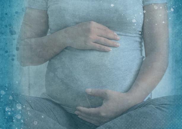 An image from the shoulders down of a mother holding her pregnant belly. She is wearing a light gray shirt and dark gray pants. There's a blue-speckled gradient filter over the image.