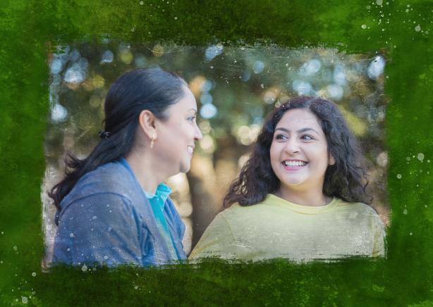 A mom and her teenage daughter smiling at each other outside.