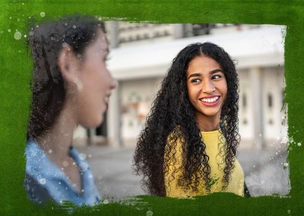 Two girls walking and smiling at one another.