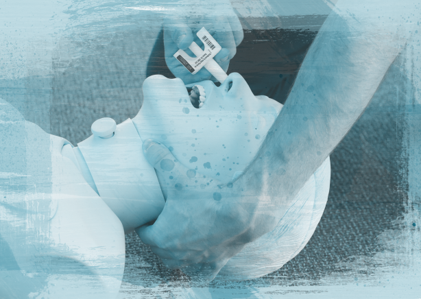 A dummy is lying on the ground. A person is holding the head of the dummy with one hand and spraying Naloxone up the dummy's nose with the other. The image is stylized with a blue film and naloxone applicators in the corners.