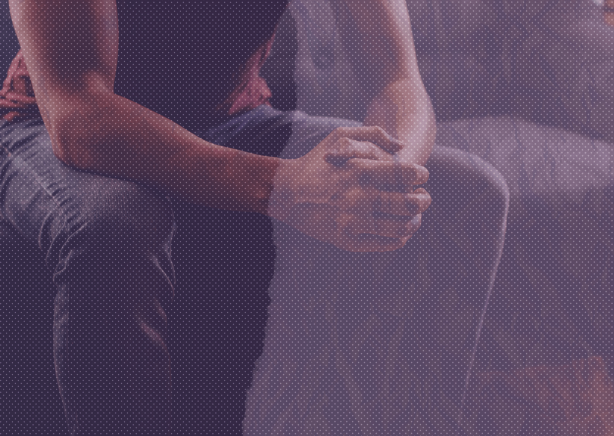  An image from the shoulders down of a person sitting on a gray couch. The image has a distressed purple tint over it with the left half of the image being darker than the right.