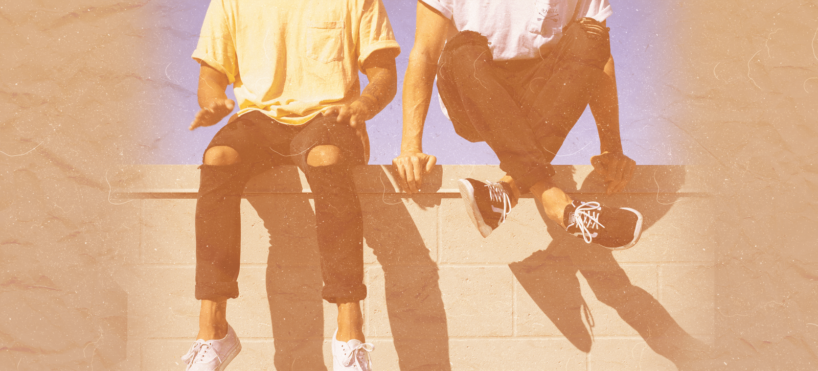 Two people sitting down on a wall.