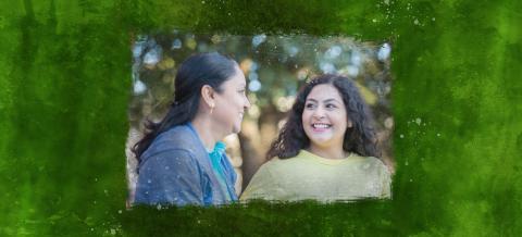 A mom and her teenage daughter smiling at each other outside.