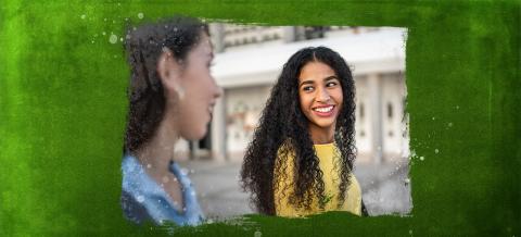 Two girls walking and smiling at one another.